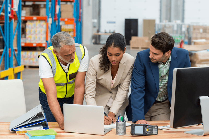 Warehouse managers and worker discussing with laptop in warehouse office