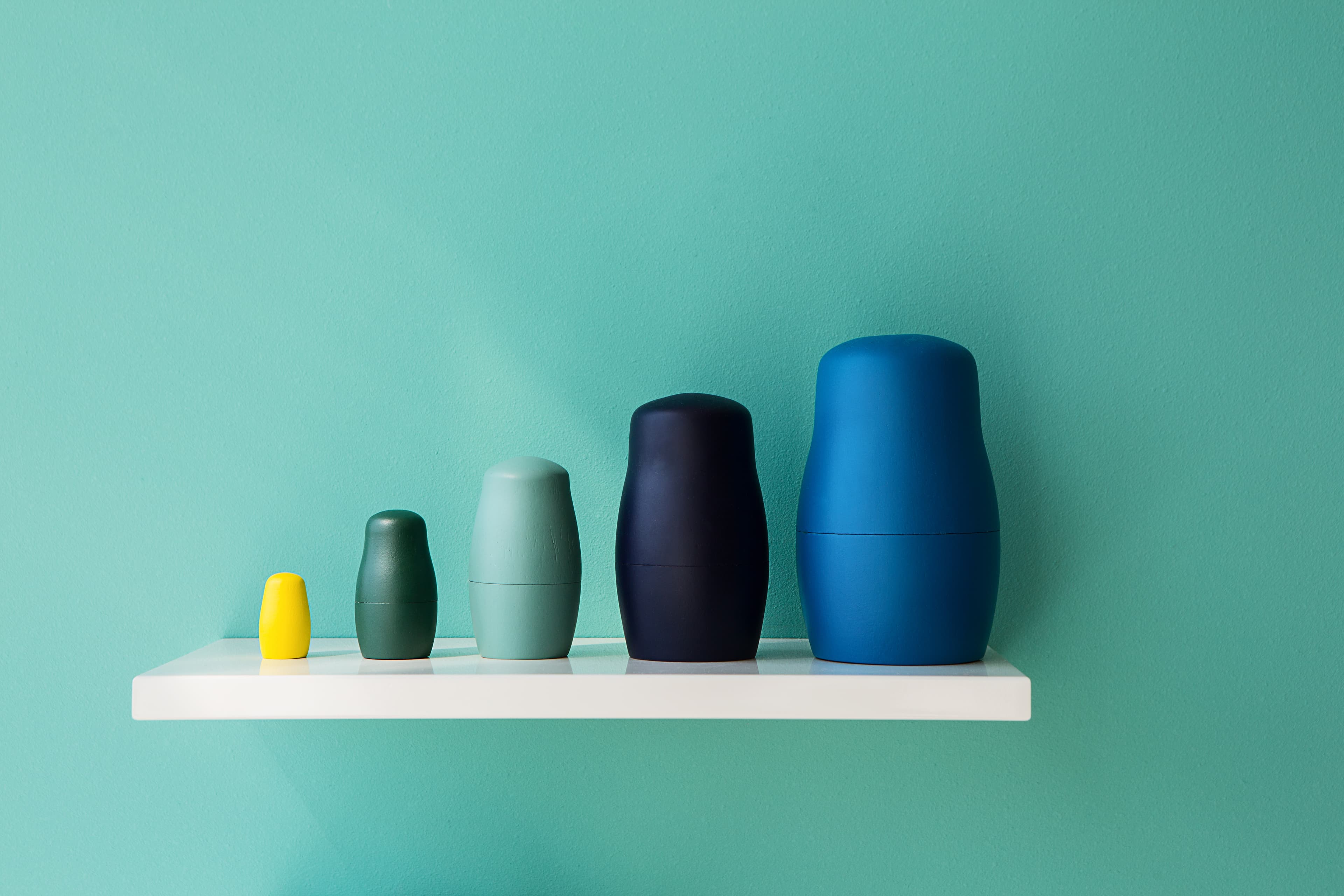 Figures toy matryoshka made in a modern style on a white shelf in one correct geometric series. Detail intrerera.