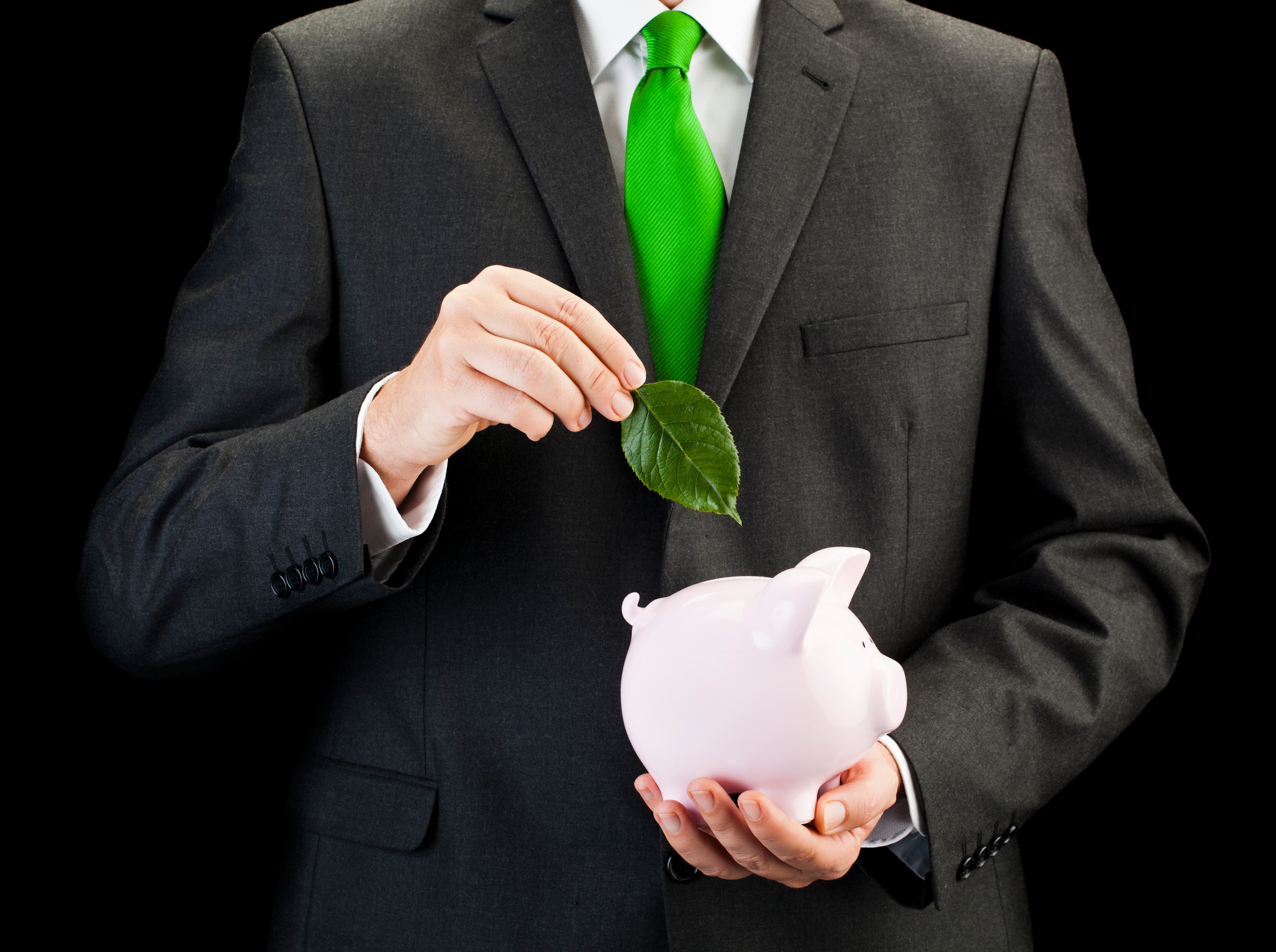 businessman putting leaf into piggy bank on black background