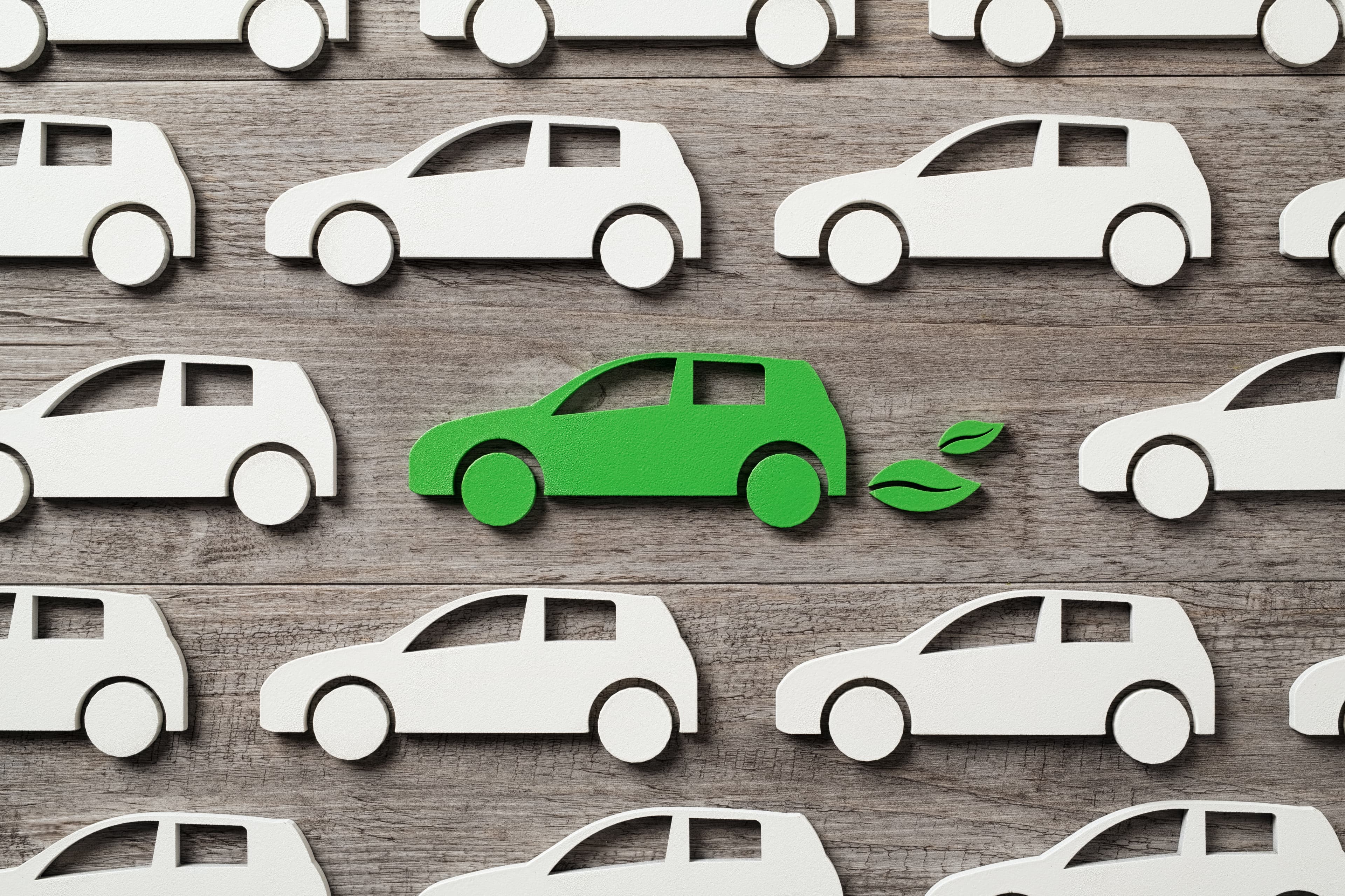Top view of green electric car with leaves symbol between polluting fossil combustion vehicles. Wooden cut out of single pollution free electric car in the middle of others. Eco friendly, clear ecology driving, no pollution and emmission free transition concept.
